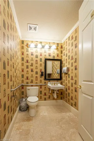 Bathroom with toilet, a textured ceiling, crown molding, and baseboards