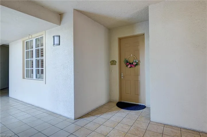 Entryway featuring a paneled door, tiled flooring, an exterior wall sconce, and a multi-pane window with interior shutters