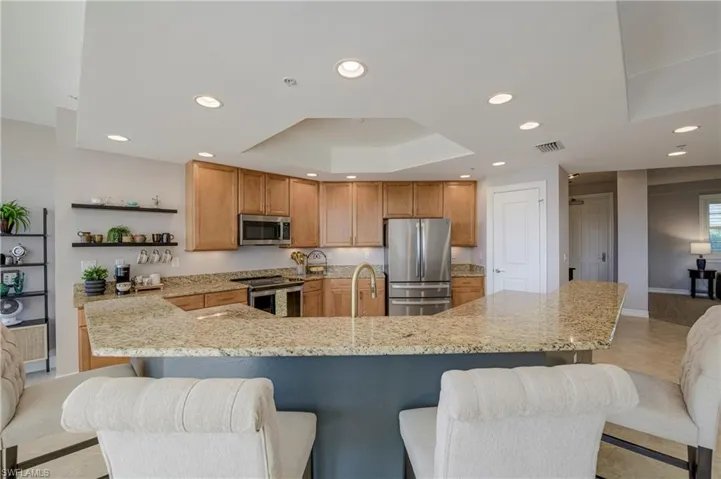 Kitchen featuring a large breakfast bar with solid surface countertops, wood cabinetry, stainless steel appliances, and recessed lighting