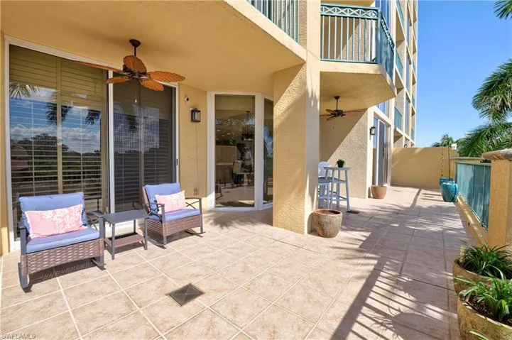 Expansive outdoor patio featuring large format tile flooring, multiple sliding glass doors, an overhead ceiling fan, and decorative railing