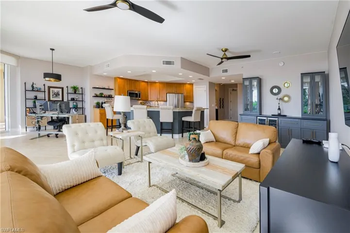 Open-concept living area with light-toned flooring, contemporary ceiling fans, and integrated kitchen and bar areas