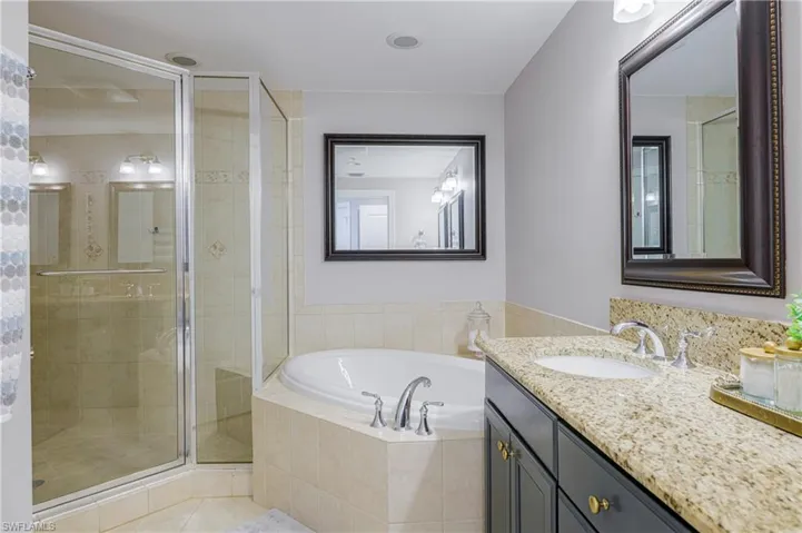 Bathroom featuring a glass-enclosed shower, a built-in corner soaking tub, a single vanity with a granite-style countertop, and tile flooring