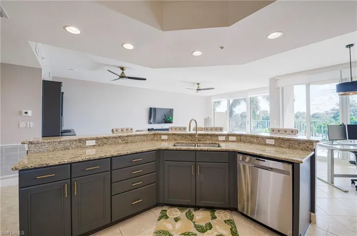 Kitchen featuring dark wood cabinetry with gold-tone hardware, a large island with a double-basin sink, stainless steel dishwasher, and stone-finish countertops