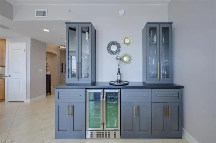 Built-in custom cabinetry with glass-front display cabinets, under-counter beverage refrigerators, contrasting dark countertop, and gold-finish hardware