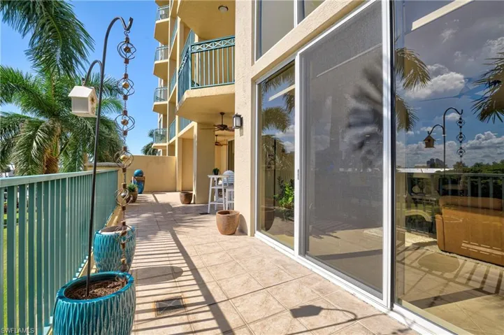 Expansive tiled balcony with a teal metal railing, featuring large sliding glass doors, exterior lighting fixtures, and a ceiling fan