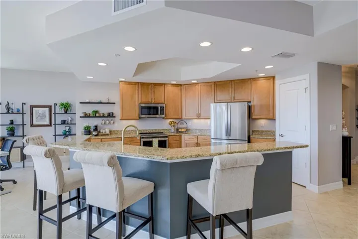 Kitchen featuring a granite-top island with seating, stainless steel appliances, wood cabinetry, and recessed lighting