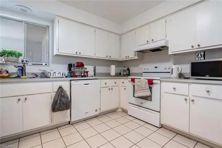 Kitchen with white appliances, white cabinetry, light countertops, under cabinet range hood, and light tile patterned floors