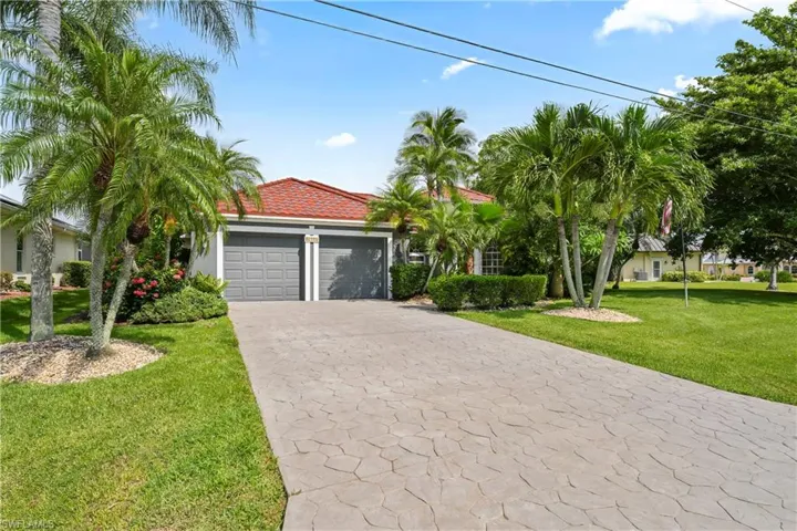 Exterior featuring a red tile roof, two-car garage, stamped concrete driveway, and mature palm trees