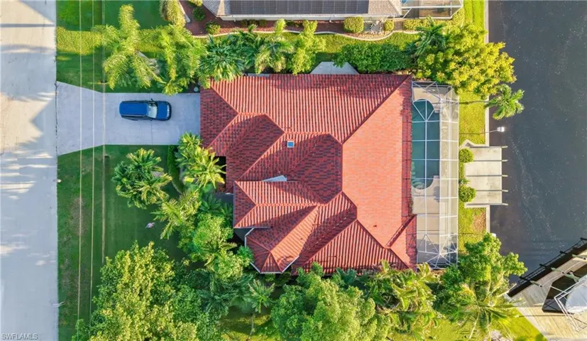 Pitched red tile roof, screened swimming pool, concrete dock, and mature landscaping