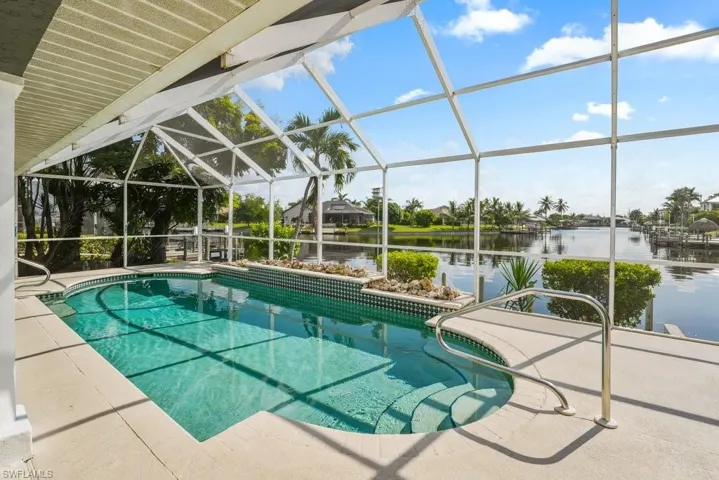 Screened pool enclosure featuring crystal-clear heated saltwater pool with lane markings, polished concrete decking, and panoramic glass panels framing waterfront vistas