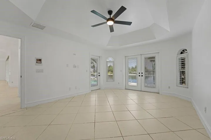 Vaulted ceiling with a ceiling fan, dual French doors, arched windows with plantation shutters, and tile flooring