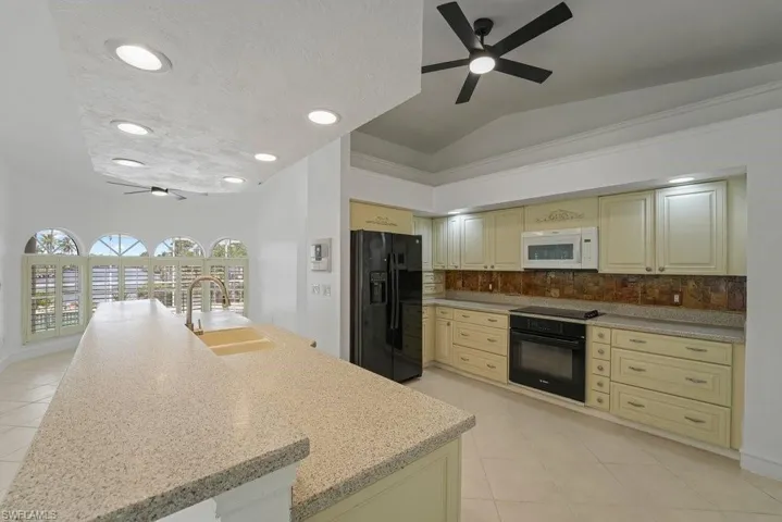 Kitchen featuring a large island with sink, light-toned cabinetry, built-in appliances, recessed lighting, and arched windows with plantation shutters