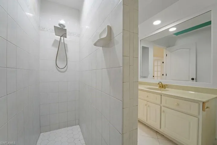 Walk-in shower with square rainfall showerhead, white tile surround, and hexagonal floor tiles