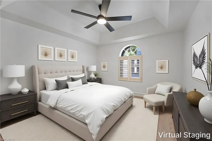 Tray ceiling, arched window with plantation shutters, ceiling fan, and wood-finish flooring