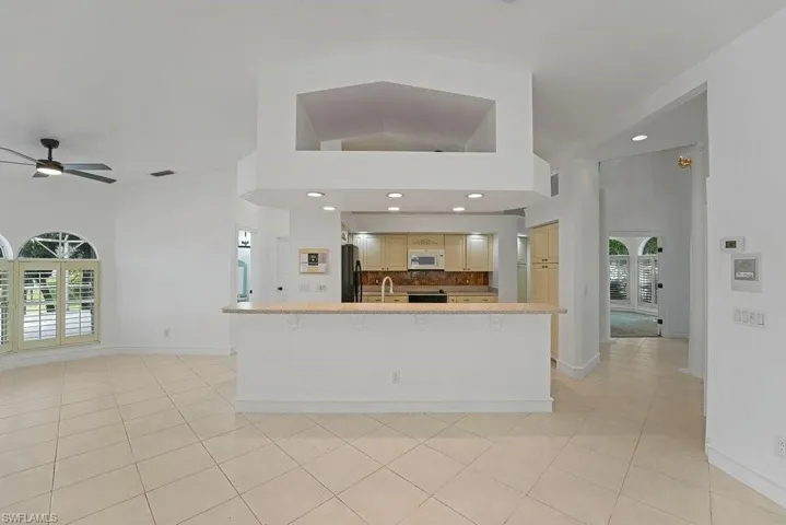Open-concept kitchen and living area featuring a large island with wood-finish countertop, recessed lighting throughout, tile flooring, and stainless steel appliances visible in the kitchen