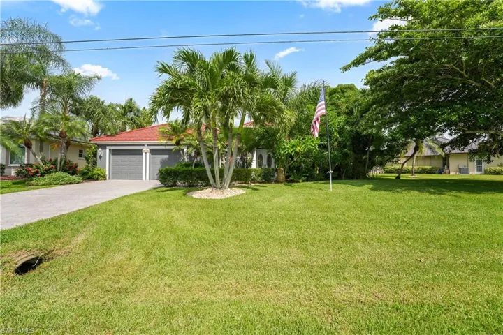 Red tile roof, dual garage doors, mature landscaping, paved driveway, and established lawn
