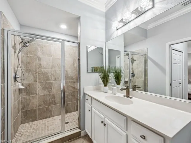 Primary bathroom featuring a shower with door, vanity, and crown molding