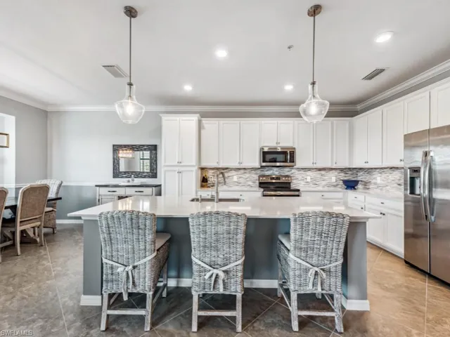 Kitchen featuring sink, white cabinets, stainless steel appliances, a center island with sink, and decorative light fixtures
