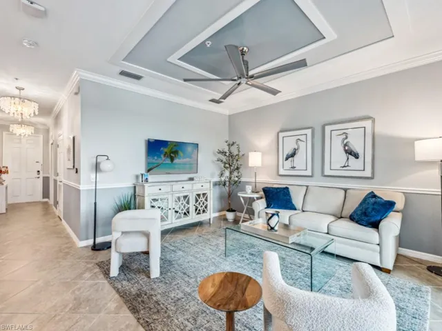 Living room featuring crown molding, ceiling fan with notable chandelier, and a tray ceiling