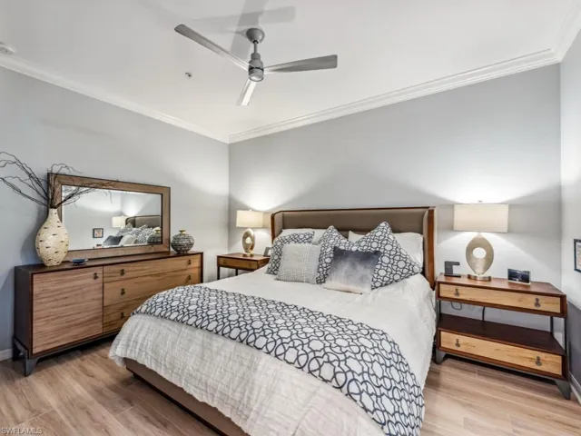 Primary bedroom with light wood-type flooring, crown molding, and ceiling fan