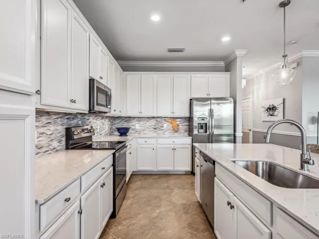 Kitchen with light stone counters, white cabinets, pendant lighting, stainless steel appliances, and sink