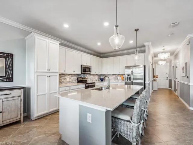 Kitchen featuring pendant lighting, white cabinetry, stainless steel appliances, crown molding, and light stone countertops