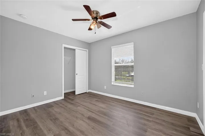 Wood-finish flooring, ceiling fan, window with blinds, and a built-in closet with bi-fold doors