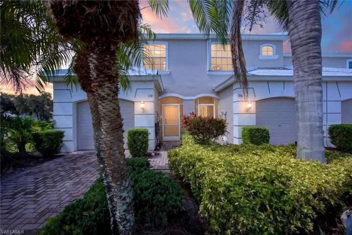 Stucco exterior with arched garage openings, paver driveway, mature palm trees, and manicured landscaping