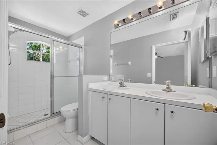 Dual vanity with integrated sinks, full-width mirror, white tile shower with sliding glass enclosure, and a window