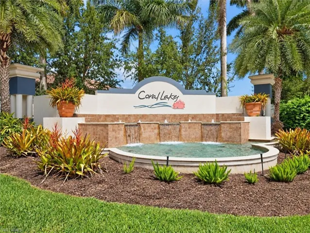 Monument sign featuring a tiered water feature with a curved basin, surrounded by lush landscaping and mature palm trees