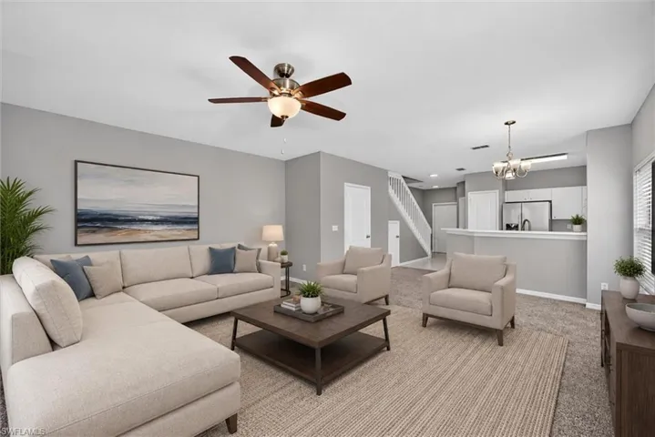 Open-concept living area featuring a ceiling fan with integrated lighting, carpeted flooring, and a kitchen pass-through
