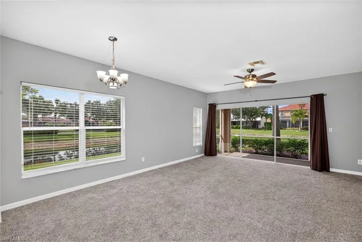 Spacious living area featuring neutral carpeting, a ceiling fan, and a chandelier