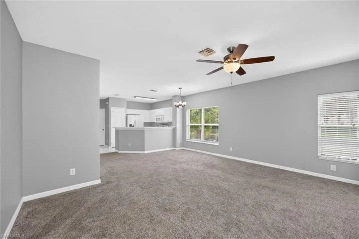 Open-concept living area with carpet flooring, a ceiling fan, and multiple windows