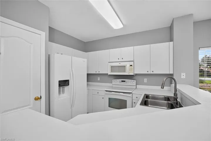White cabinetry, white appliances, dual basin stainless steel sink, and light-toned countertops