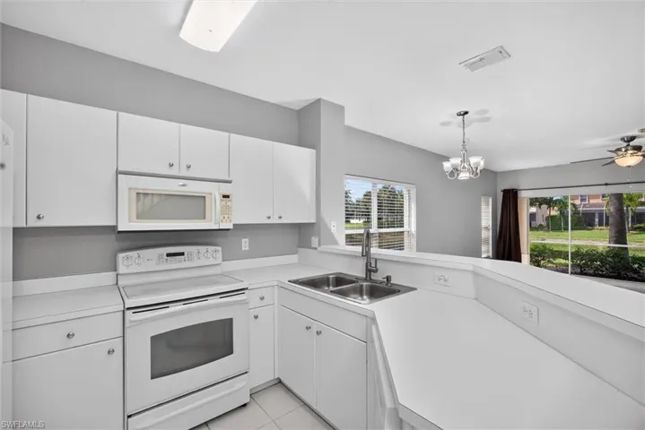 White cabinetry with coordinating countertops, stainless steel sink with a high-arc faucet, and an electric range with an overhead microwave