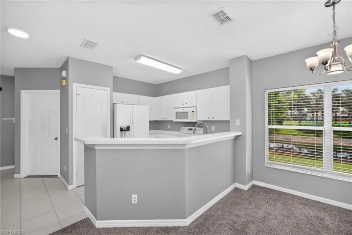 Modern kitchen featuring a curved island with white cabinetry, stainless steel appliances, recessed ceiling lighting, ceramic tile flooring, and large multi-pane windows with plantation shutters overlooking the grounds