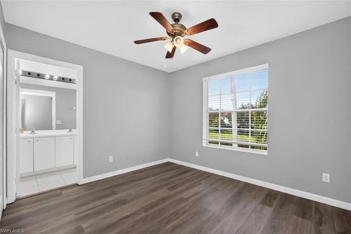 Wood-finish flooring, ceiling fan with integrated lighting, window with horizontal blinds, and an attached vanity space with dual sinks and overhead lighting