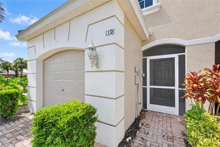 Stucco exterior featuring an arched garage entrance, decorative outdoor lighting, a screened entry, and a brick paver pathway