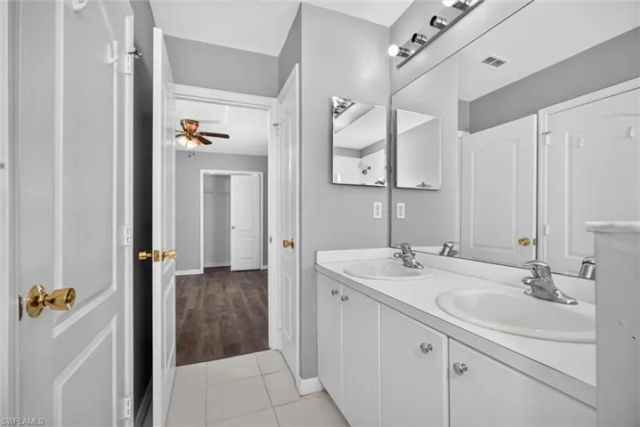 Dual sink vanity with white cabinetry, light gray wall paint, and a large wall-mounted mirror