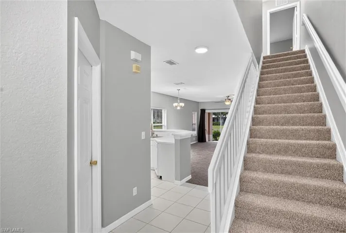 Two-story interior featuring a carpeted staircase with white railings, tile flooring, and neutral wall paint