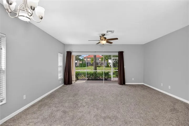 Expansive room featuring neutral-toned carpet flooring, light gray wall paint, and a ceiling fan