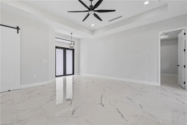 Unfurnished room with french doors, ceiling fan, a raised ceiling, and a barn door