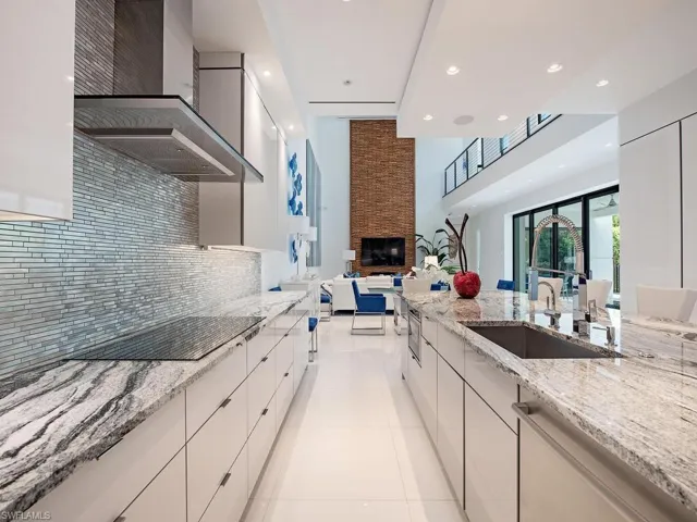Kitchen featuring light stone counters, wall chimney range hood, a fireplace, white cabinetry, and stainless steel dishwasher