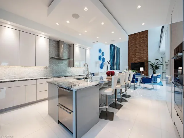 Kitchen featuring an island with sink, backsplash, light tile floors, wall chimney exhaust hood, and a kitchen bar
