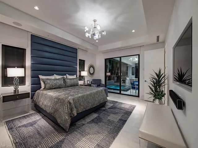 Bedroom featuring a tray ceiling, an inviting chandelier, light wood-type flooring, and access to exterior
