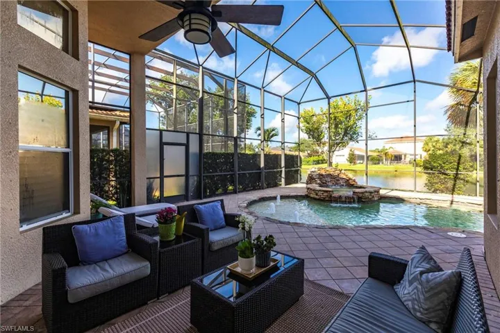 View of patio / terrace featuring a pool with connected hot tub, ceiling fan, a water view, and glass enclosure