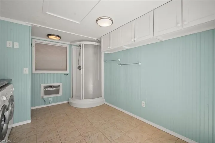 Laundry room with washer and clothes dryer, laundry area, light tile patterned floors, baseboards, and an AC wall unit