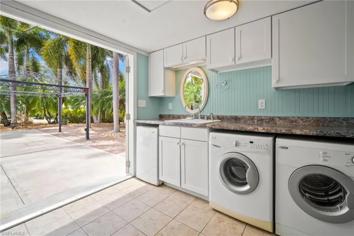 Clothes washing area with cabinet space, a sink, separate washer and dryer, and light tile patterned floors