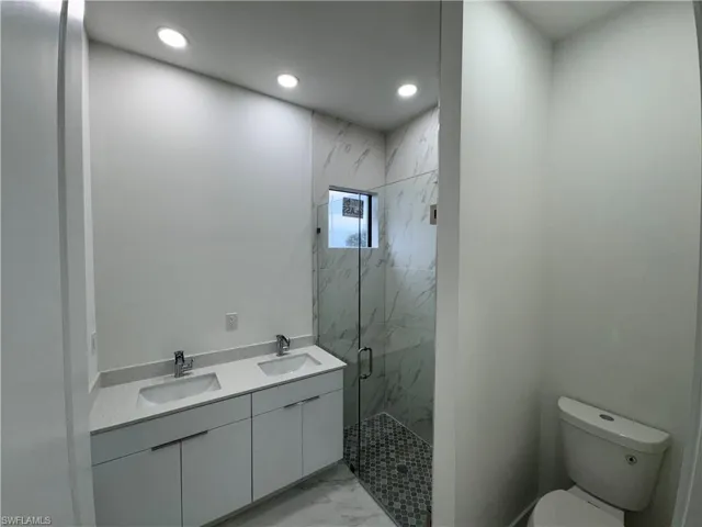 Bathroom with a marble finish shower, double vanity, recessed lighting, and light marble finish flooring