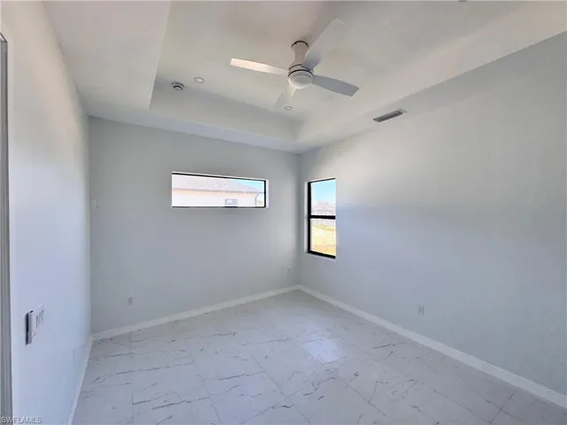 Unfurnished room with a tray ceiling, plenty of natural light, and a ceiling fan